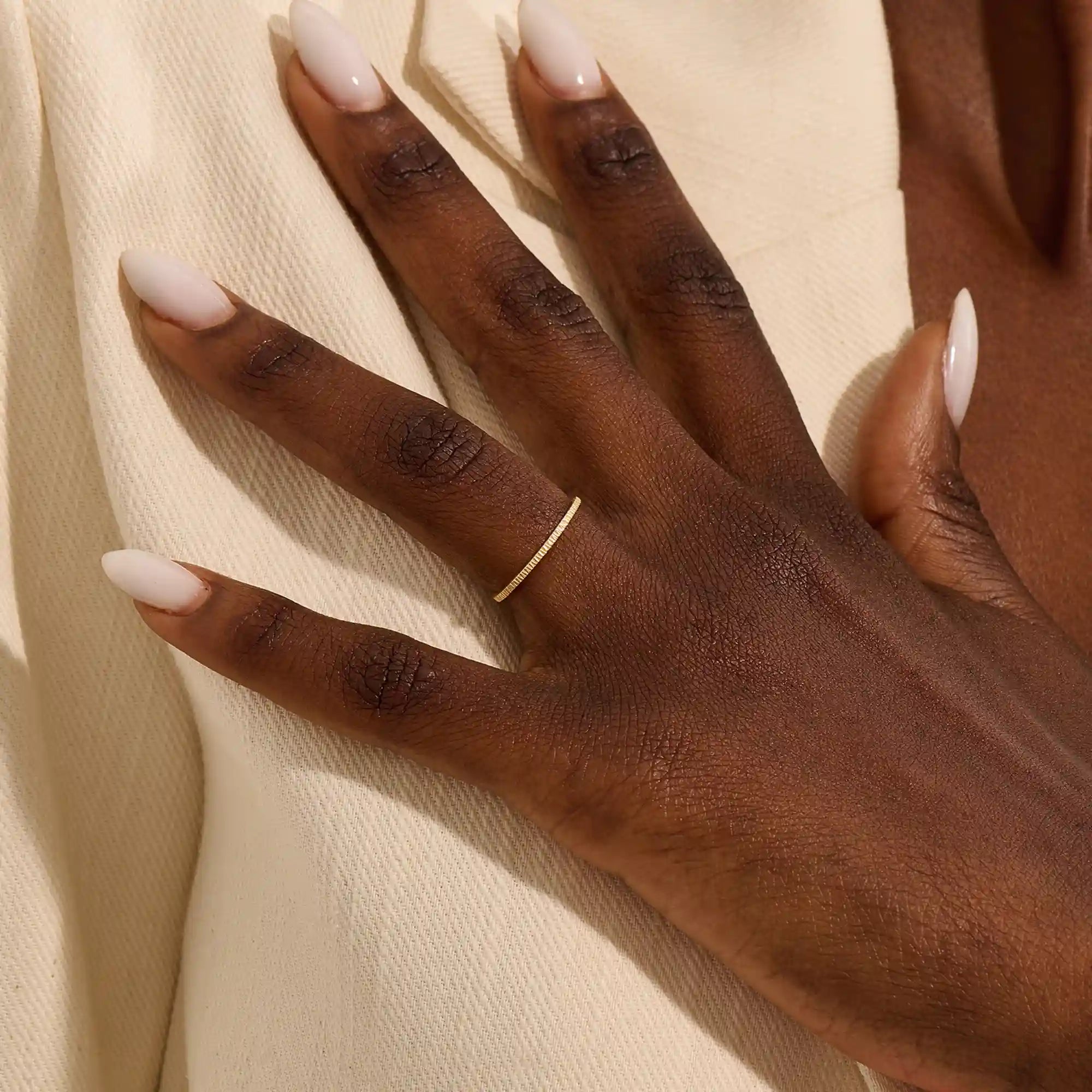 Close-up of a woman wearing a 14k solid yellow gold thin stacking ring with faceted textured design, minimal and elegant everyday jewelry
