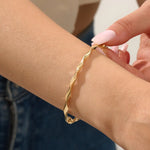 Close-up of a woman wearing a 14k solid yellow gold twist bangle bracelet, showing the bracelet’s sculpted wave design glimmering in natural light.
