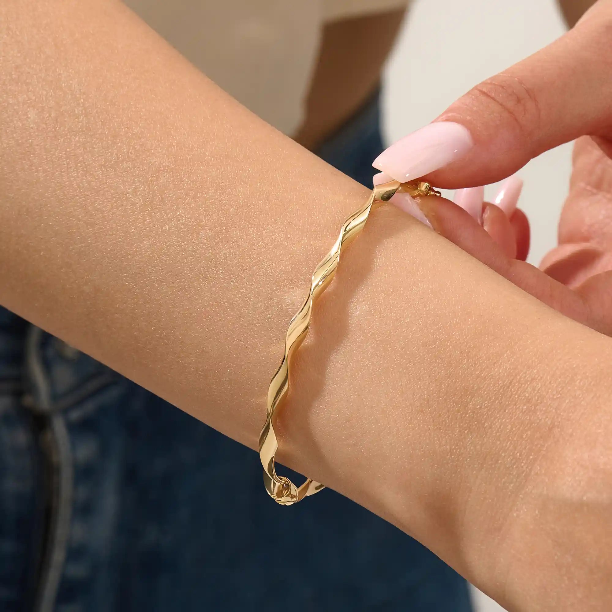 Close-up of a woman wearing a 14k solid yellow gold twist bangle bracelet, showing the bracelet’s sculpted wave design glimmering in natural light.
