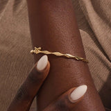 Close-up of a woman wearing a 14k solid yellow gold twist bangle bracelet, showing the bracelet’s sculpted wave design glimmering in natural light.
