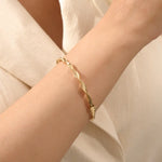 Close-up of a woman wearing a 14k solid yellow gold twist bangle bracelet, showing the bracelet’s sculpted wave design glimmering in natural light.
