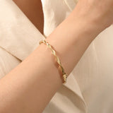 Close-up of a woman wearing a 14k solid yellow gold twist bangle bracelet, showing the bracelet’s sculpted wave design glimmering in natural light.
