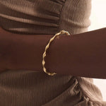 Close-up of a woman wearing a 14k solid yellow gold twist bangle bracelet, showing the bracelet’s sculpted wave design glimmering in natural light.
