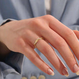 Close-up of a woman wearing a 14k solid yellow gold twist eternity wedding band with moissanites set in a sculpted design all around
