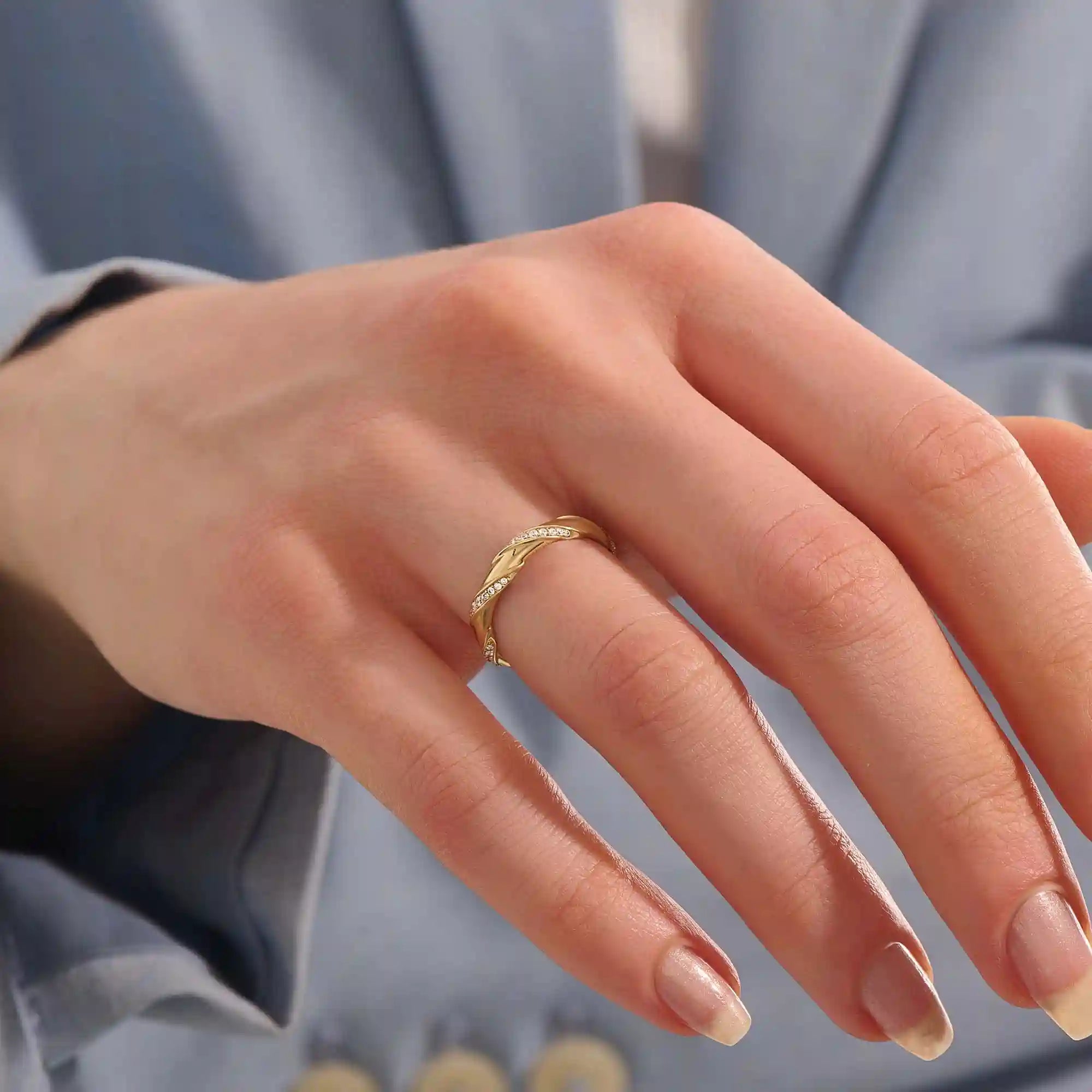 Close-up of a woman wearing a 14k solid yellow gold twist eternity wedding band with moissanites set in a sculpted design all around
