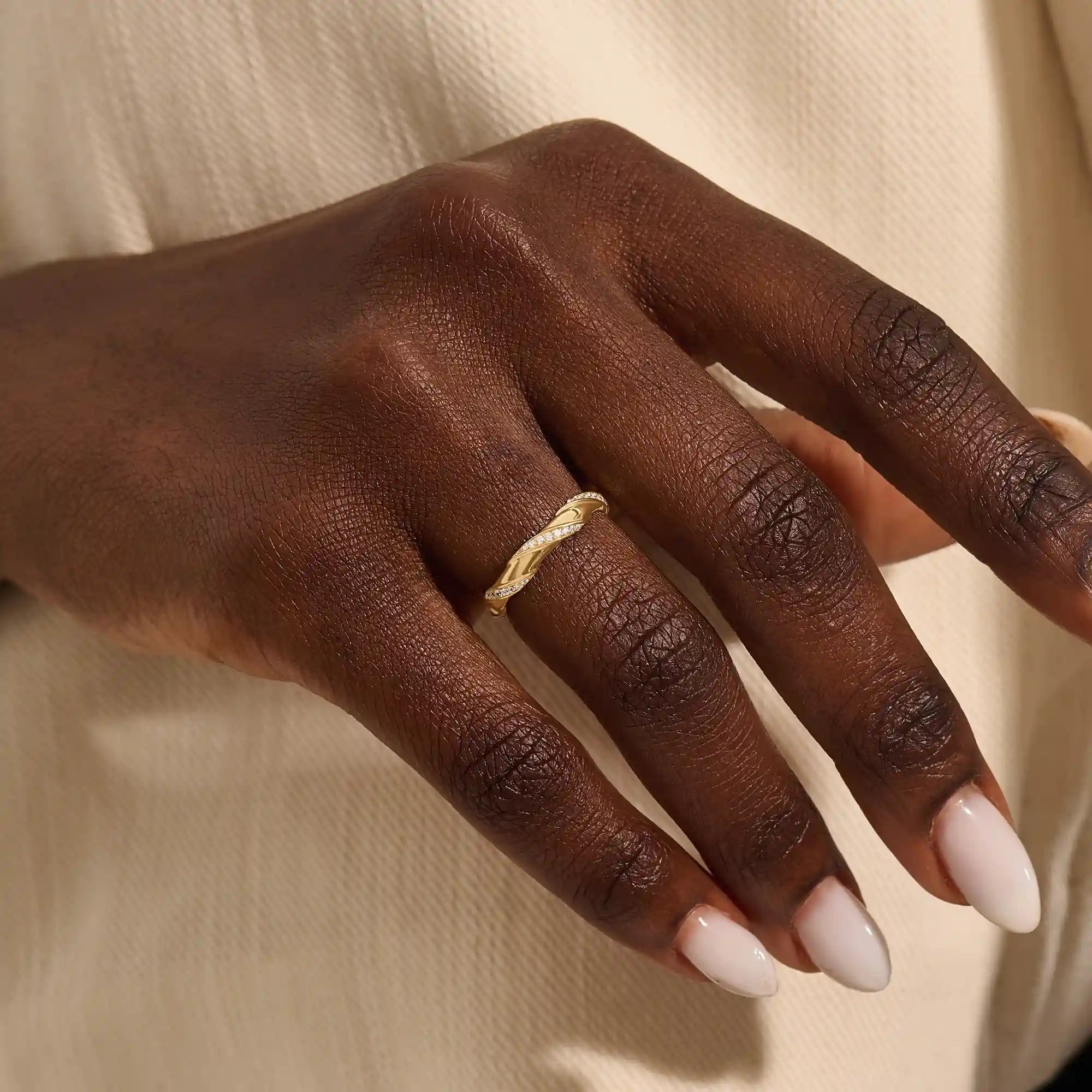 Close-up of a woman wearing a 14k solid yellow gold twist eternity wedding band with moissanites set in a sculpted design all around
