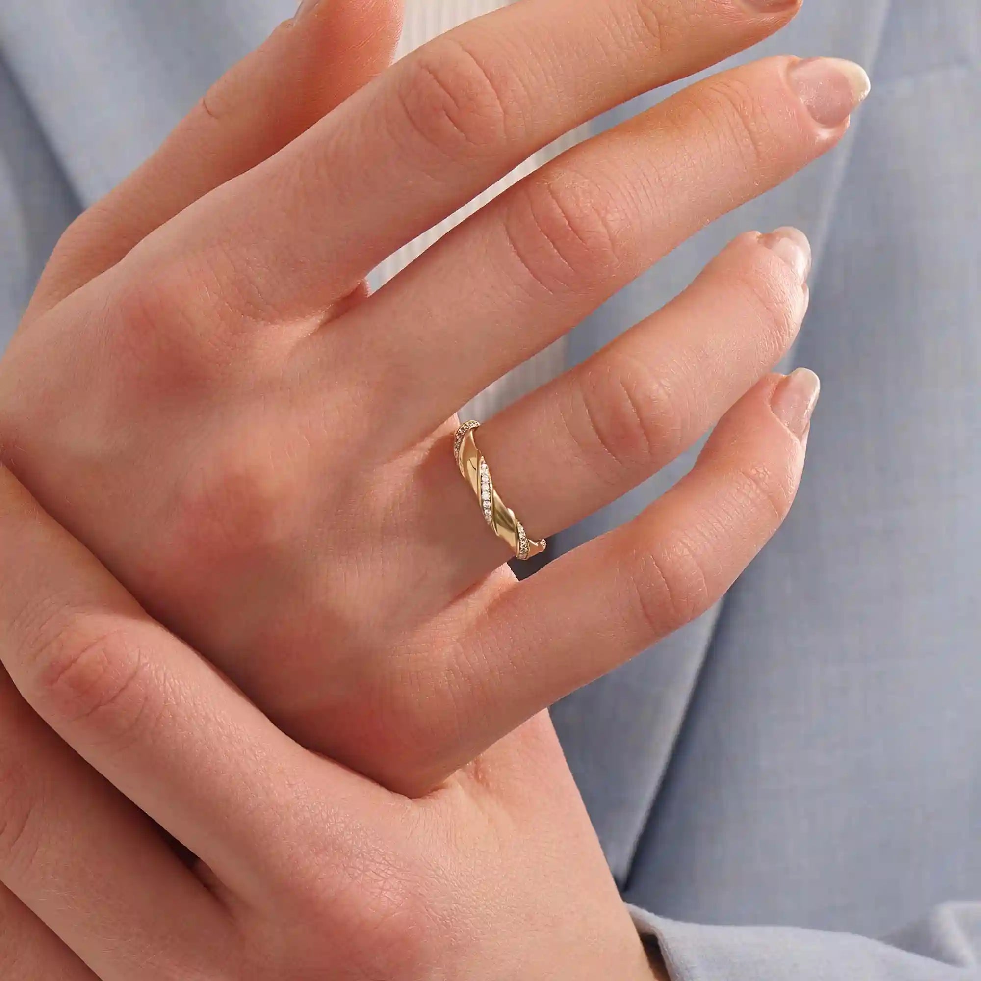 Close-up of a woman wearing a 14k solid yellow gold twist eternity wedding band with moissanites set in a sculpted design all around
