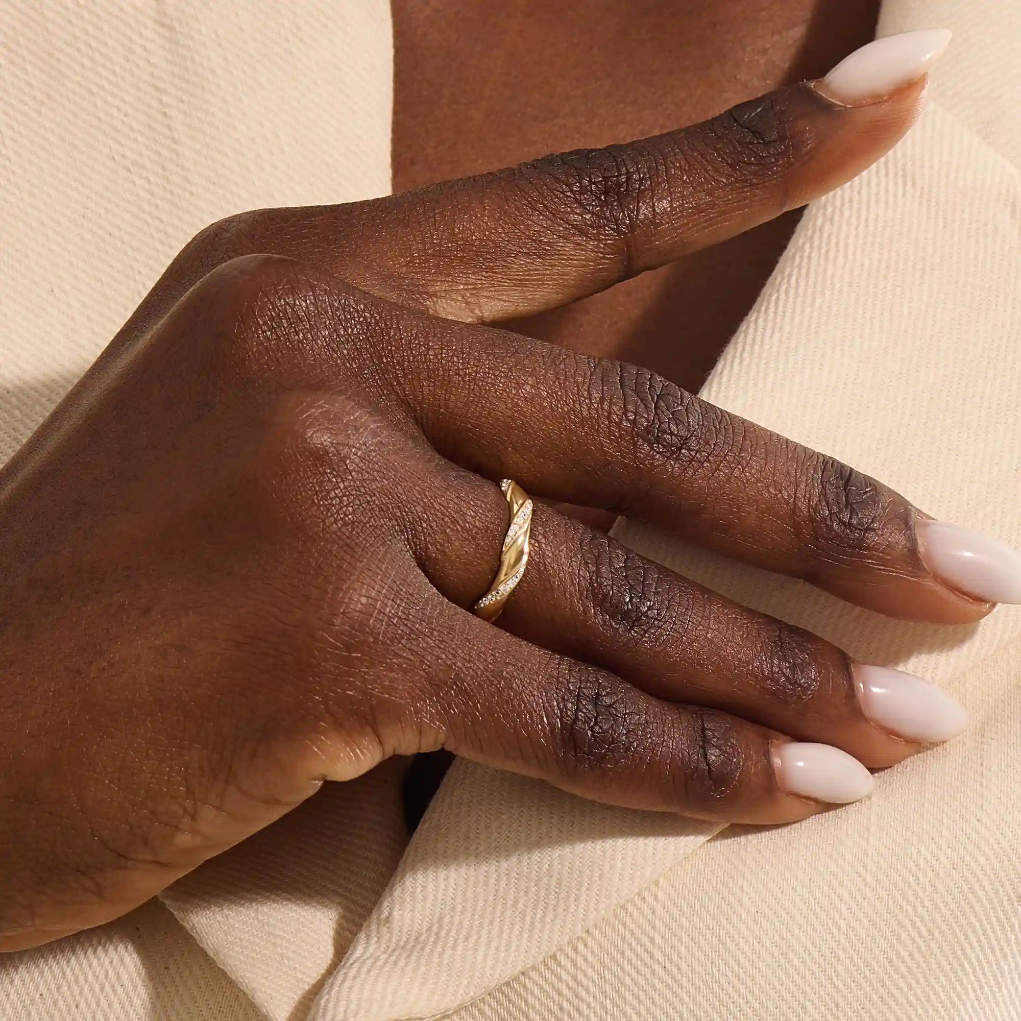 Close-up of a woman wearing a 14k solid yellow gold twist eternity wedding band with moissanites set in a sculpted design all around
