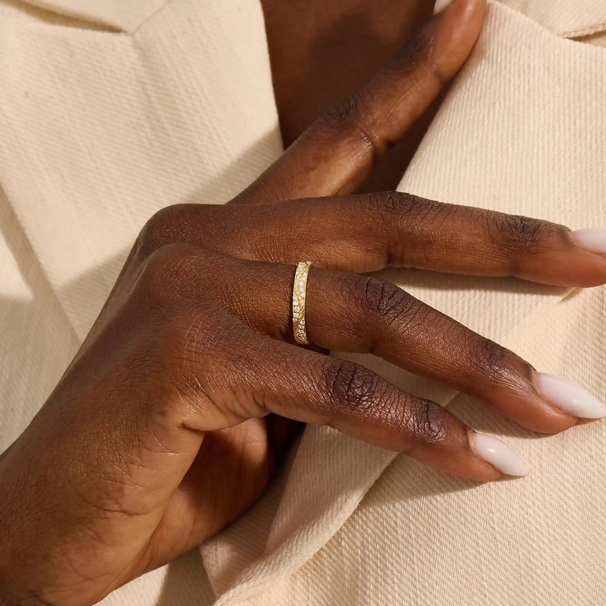 Close-up of a woman wearing a 14k solid yellow gold twisted eternity wedding band with sparkling moissanites in a continuous setting
