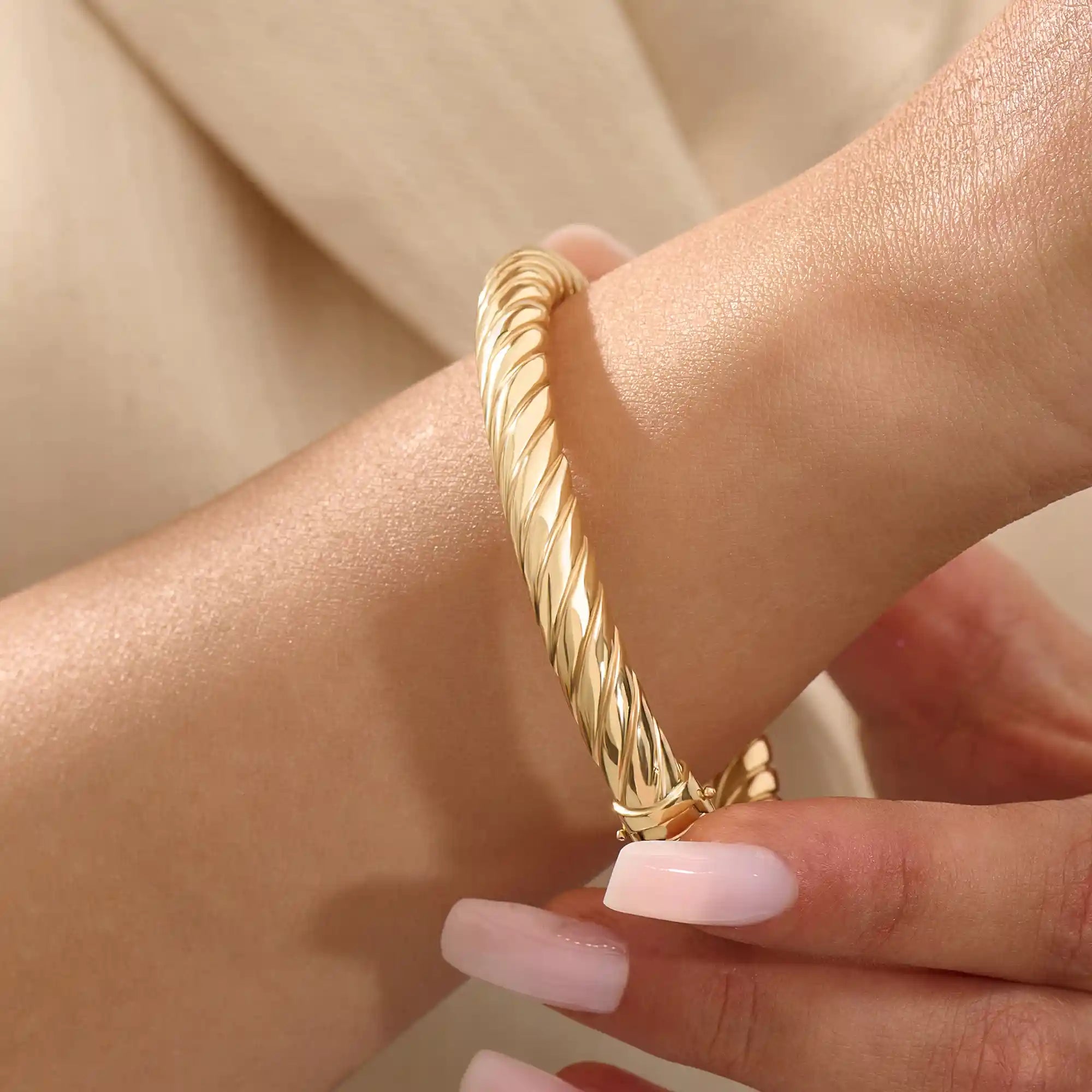 Close-up of a woman wearing a 14k solid yellow gold twisted rope bangle, styled alone to highlight its bold, sculptural form and gleaming polish.
