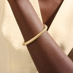 Close-up of a woman wearing a 14k solid yellow gold twisted rope bangle, styled alone to highlight its bold, sculptural form and gleaming polish.
