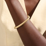 Close-up of a woman wearing a 14k solid yellow gold twisted rope bangle, styled alone to highlight its bold, sculptural form and gleaming polish.
