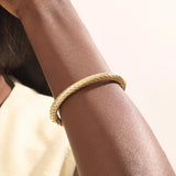 Close-up of a woman wearing a 14k solid yellow gold twisted rope bangle, styled alone to highlight its bold, sculptural form and gleaming polish.
