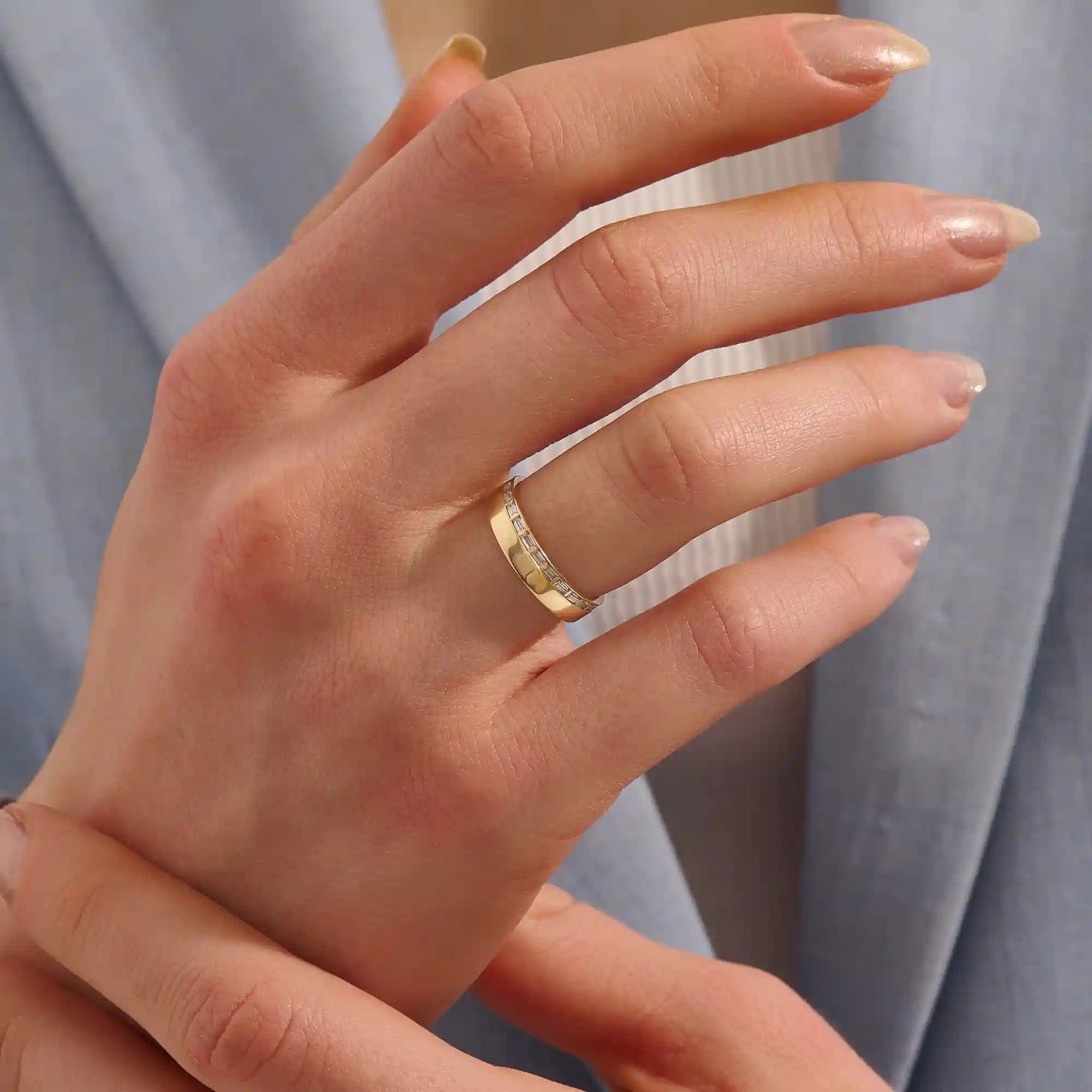 Close-up of a woman wearing a 14k solid yellow gold wide wedding band with baguette moissanite stones in an eternity design
