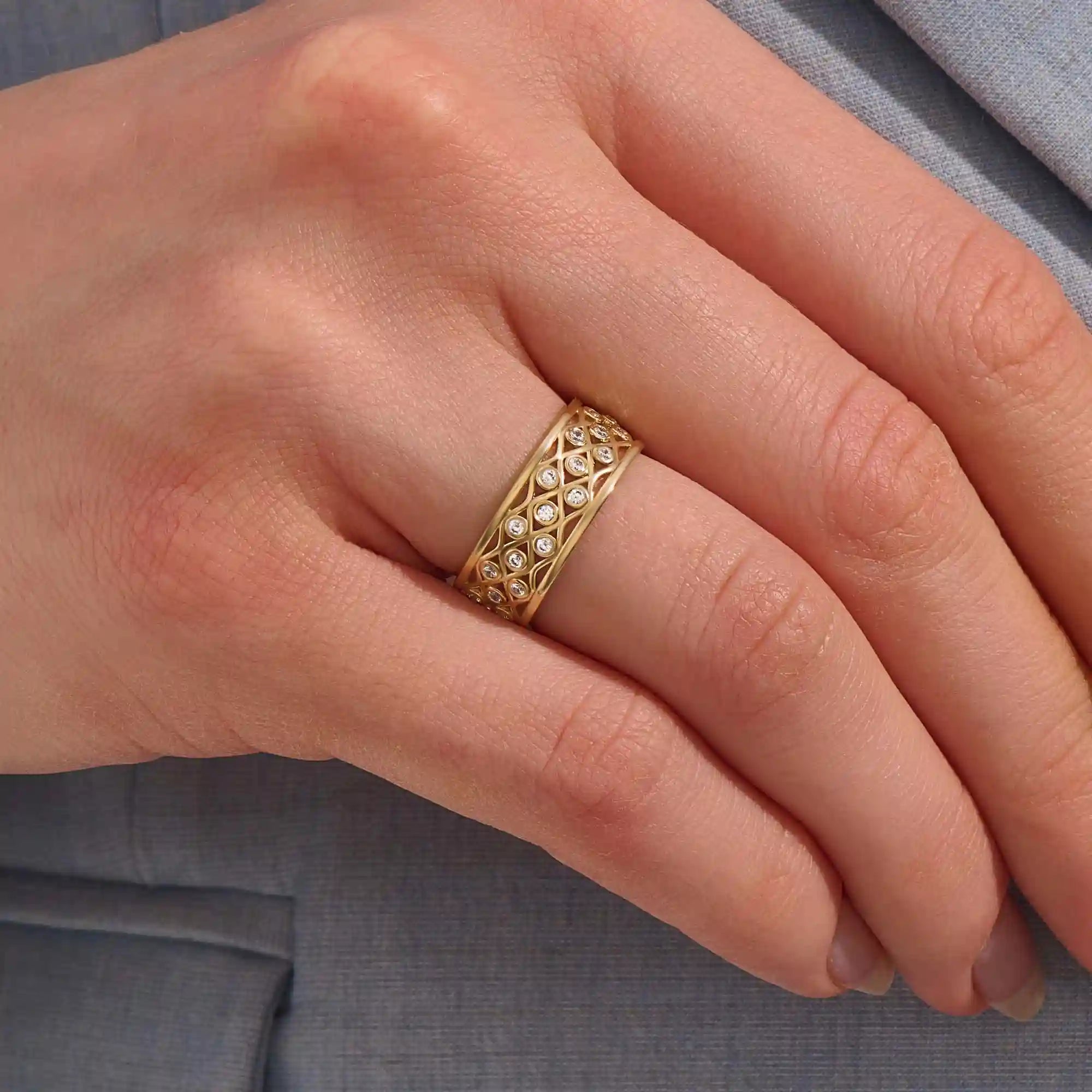Close-up of a woman wearing a 14k solid yellow gold wide wedding band with moissanite stones in an open lattice setting
