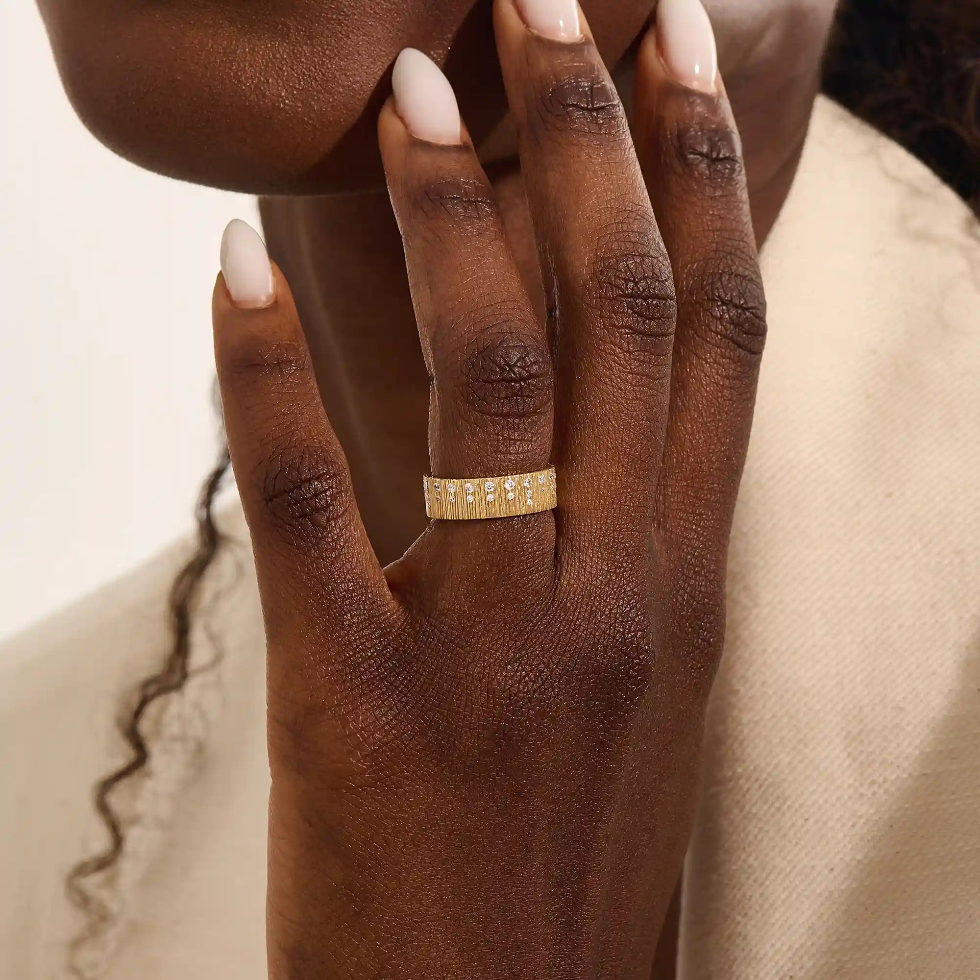Close-up of a woman wearing a 14k solid yellow gold wide wedding band with wood grain texture and pavé set round brilliant cut moissanite stones, distinctive and modern statement jewelry
