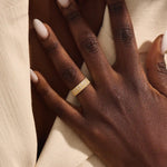 Close-up of a woman wearing a 14k solid yellow gold wide wedding band with wood grain texture and pavé set round brilliant cut moissanite stones, distinctive and modern statement jewelry
