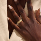 Close-up of a woman wearing a 14k solid yellow gold wide wedding band with wood grain texture and pavé set round brilliant cut moissanite stones, distinctive and modern statement jewelry
