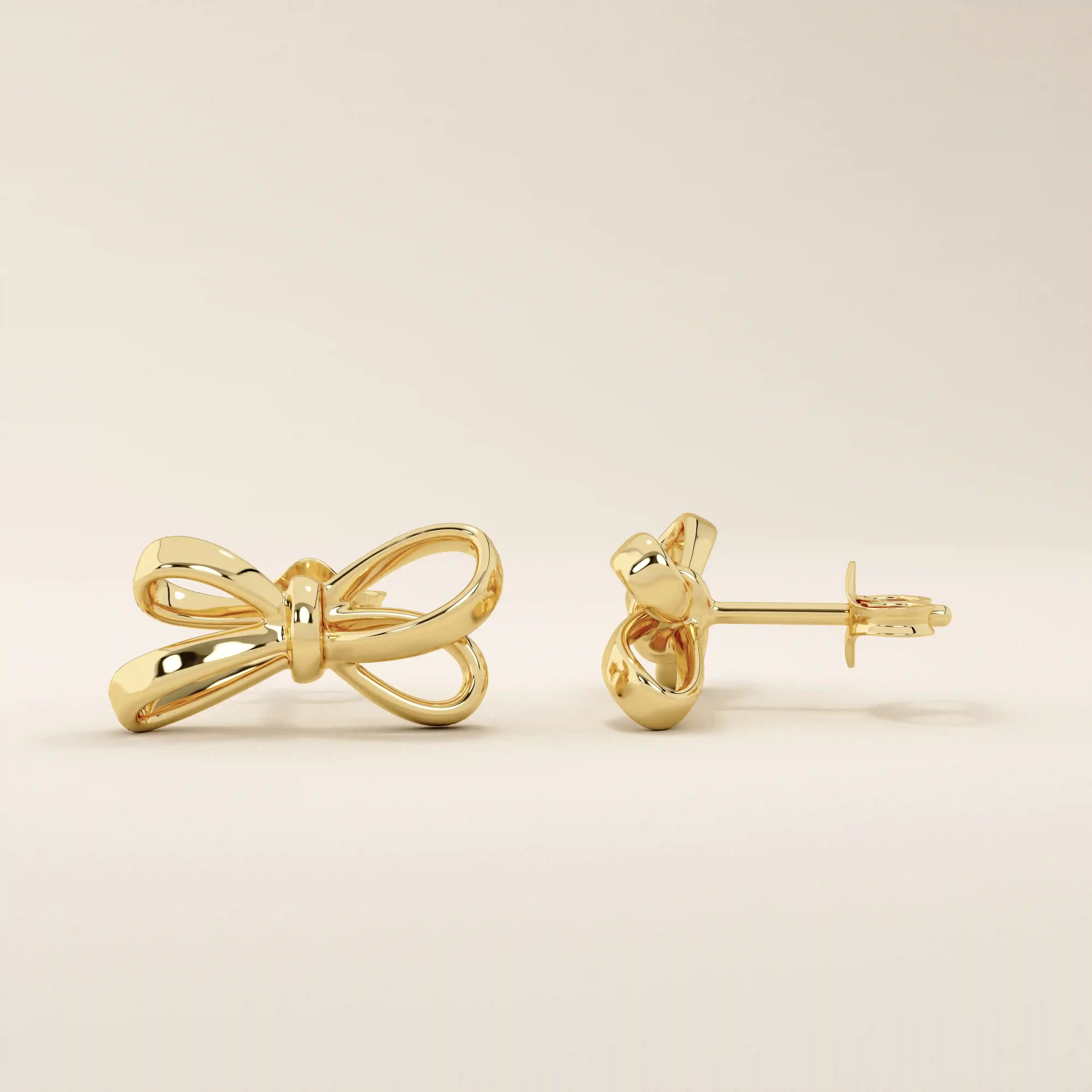 Close-up of simple ribbon stud earrings in polished 14k gold featuring a graceful bow silhouette.

