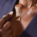 Model showcases a bold pavé initial necklace in 14k gold, sparkling with moissanite stones. Perfect for layering or gifting with impact.