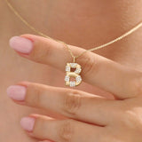 Model showcases a bold pavé initial necklace in 14k gold, sparkling with moissanite stones. Perfect for layering or gifting with impact.