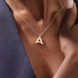Model showcases a bold pavé initial necklace in 14k gold, sparkling with moissanite stones. Perfect for layering or gifting with impact.