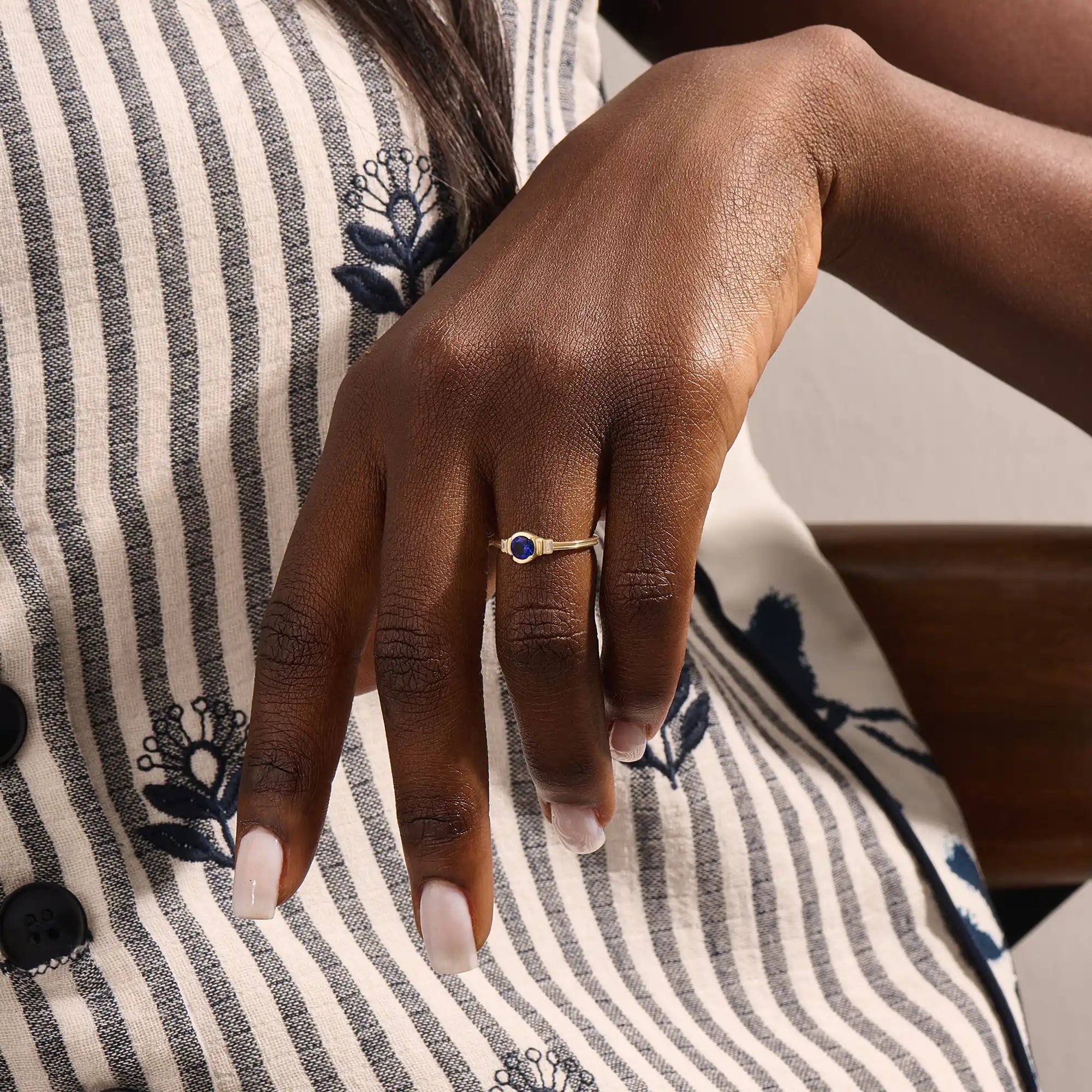 Model wearing a 14k gold anniversary ring with round sapphire and baguette moissanite stones. Sleek, timeless design for special occasions.