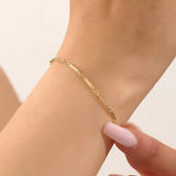 Model wearing a 14k gold bracelet with flat bar segments linked by oval chain for a modern minimalist look.
