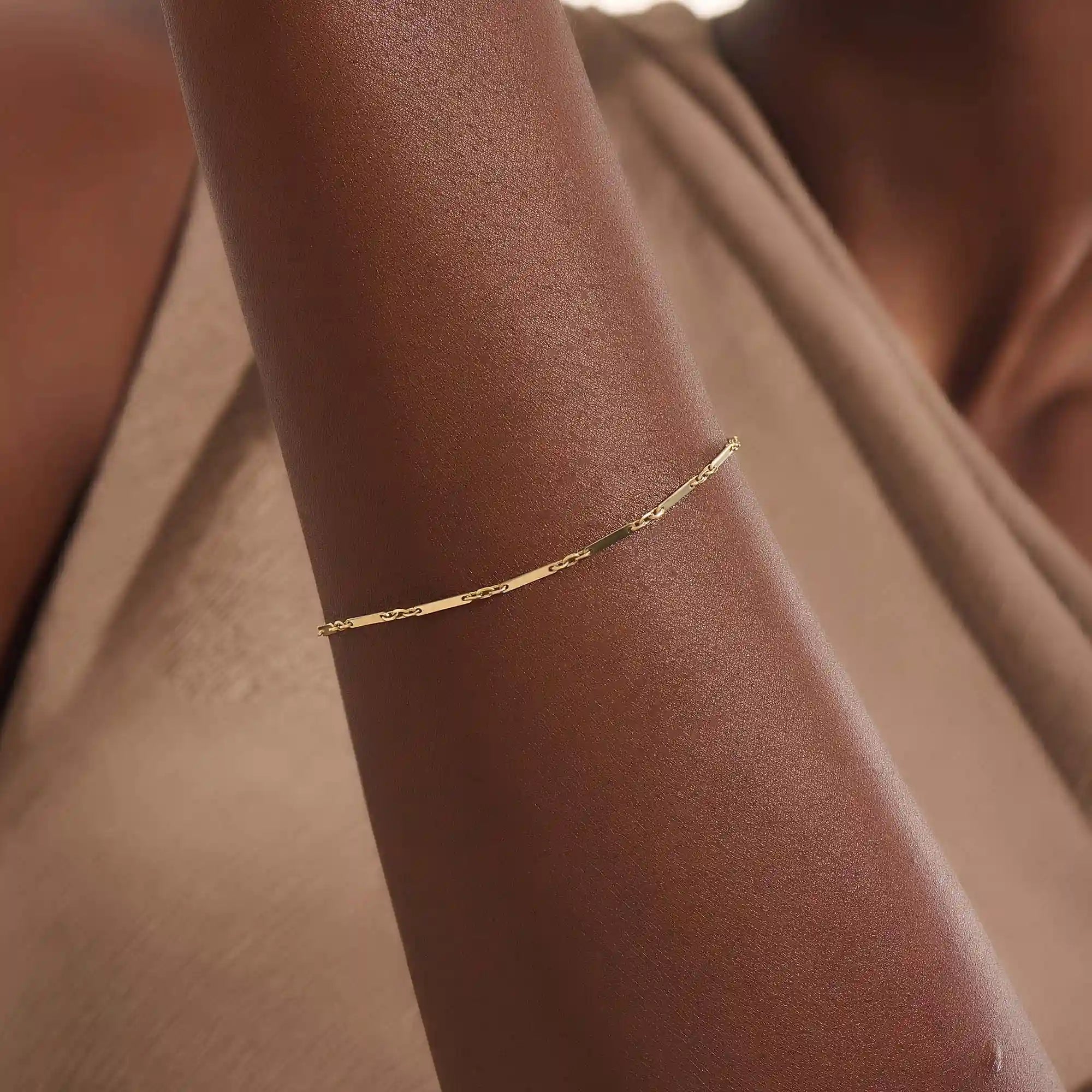 Model wearing a 14k gold bracelet with flat bar segments linked by oval chain for a modern minimalist look.
