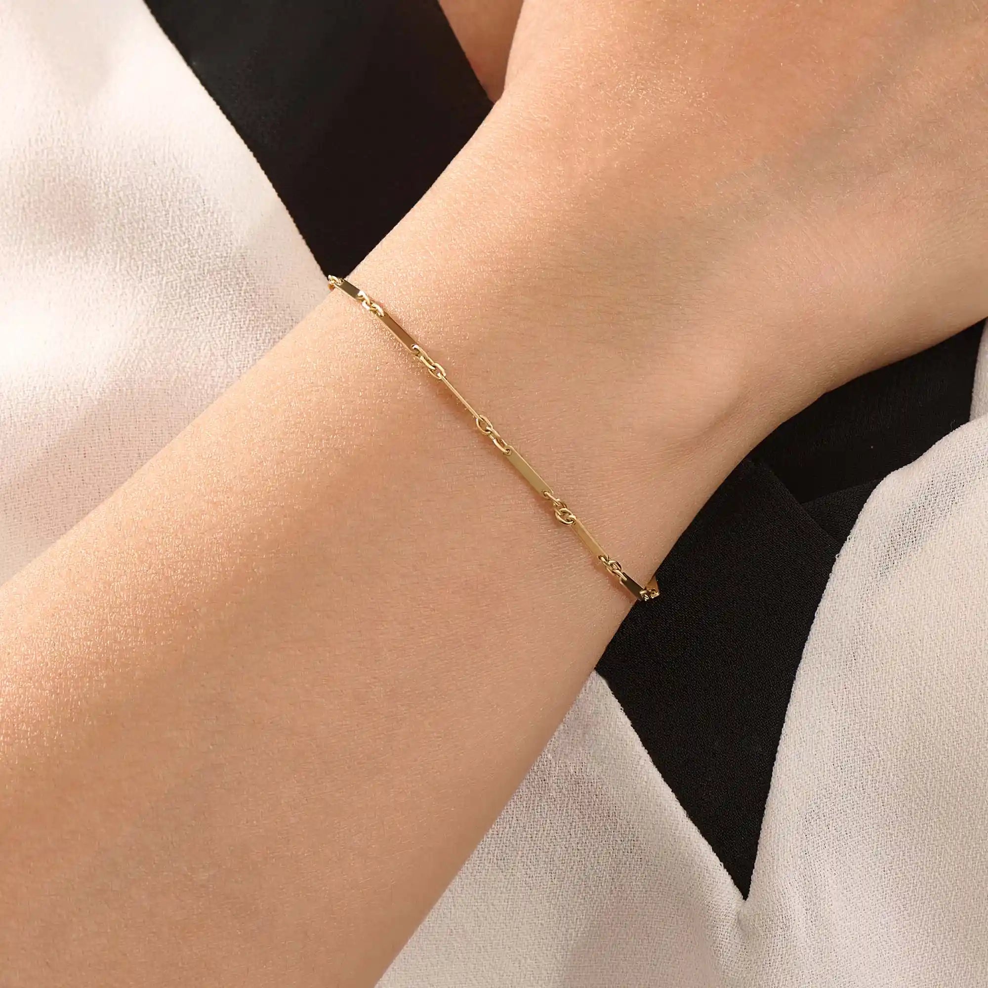 Model wearing a 14k gold bracelet with flat bar segments linked by oval chain for a modern minimalist look.
