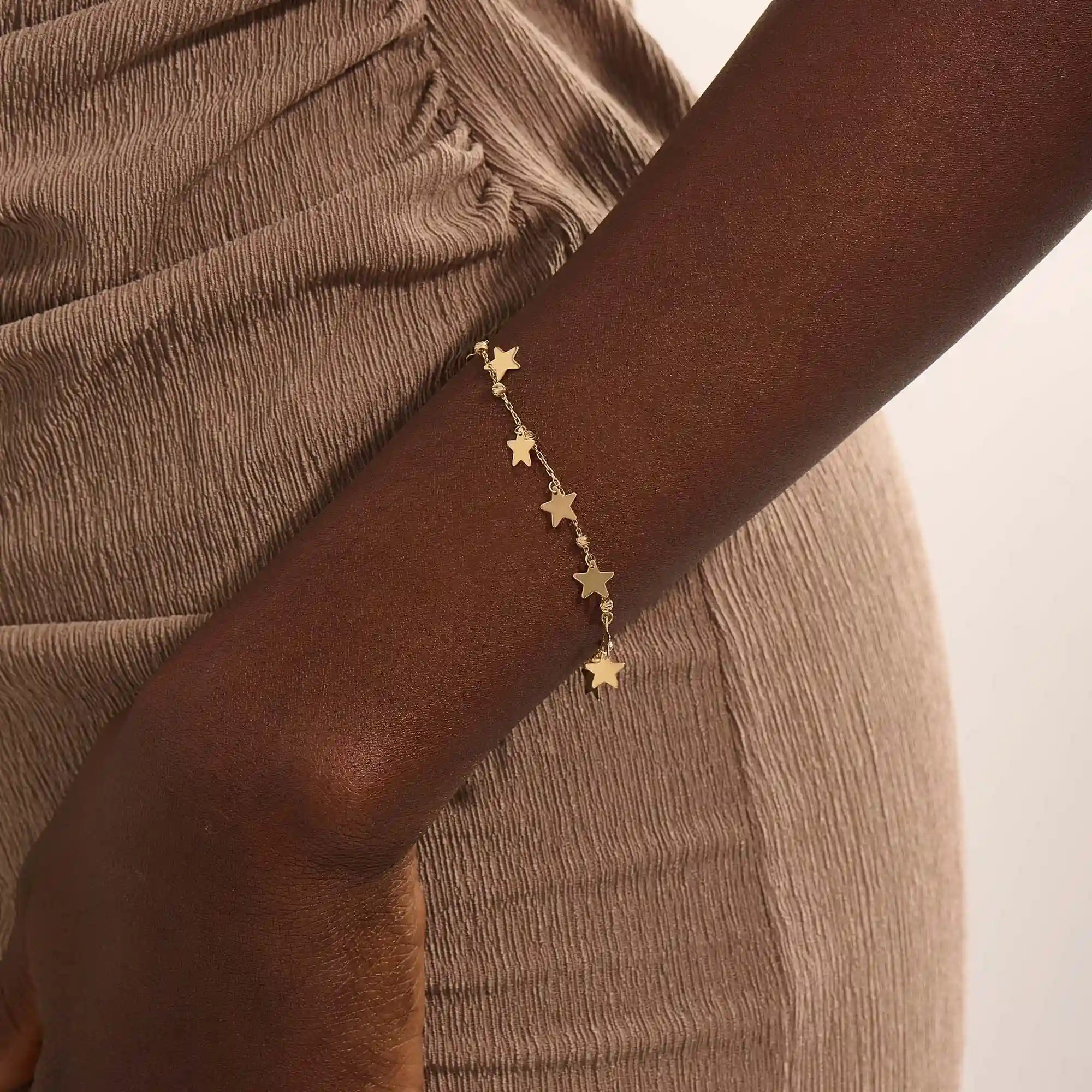 Model wearing a 14k gold dangling star bracelet with hanging charms, adding a whimsical and elegant touch.
