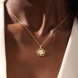Model wearing a 14k gold flower pendant necklace with an engravable plain surface. A delicate and personalized accessory ideal for daily wear.