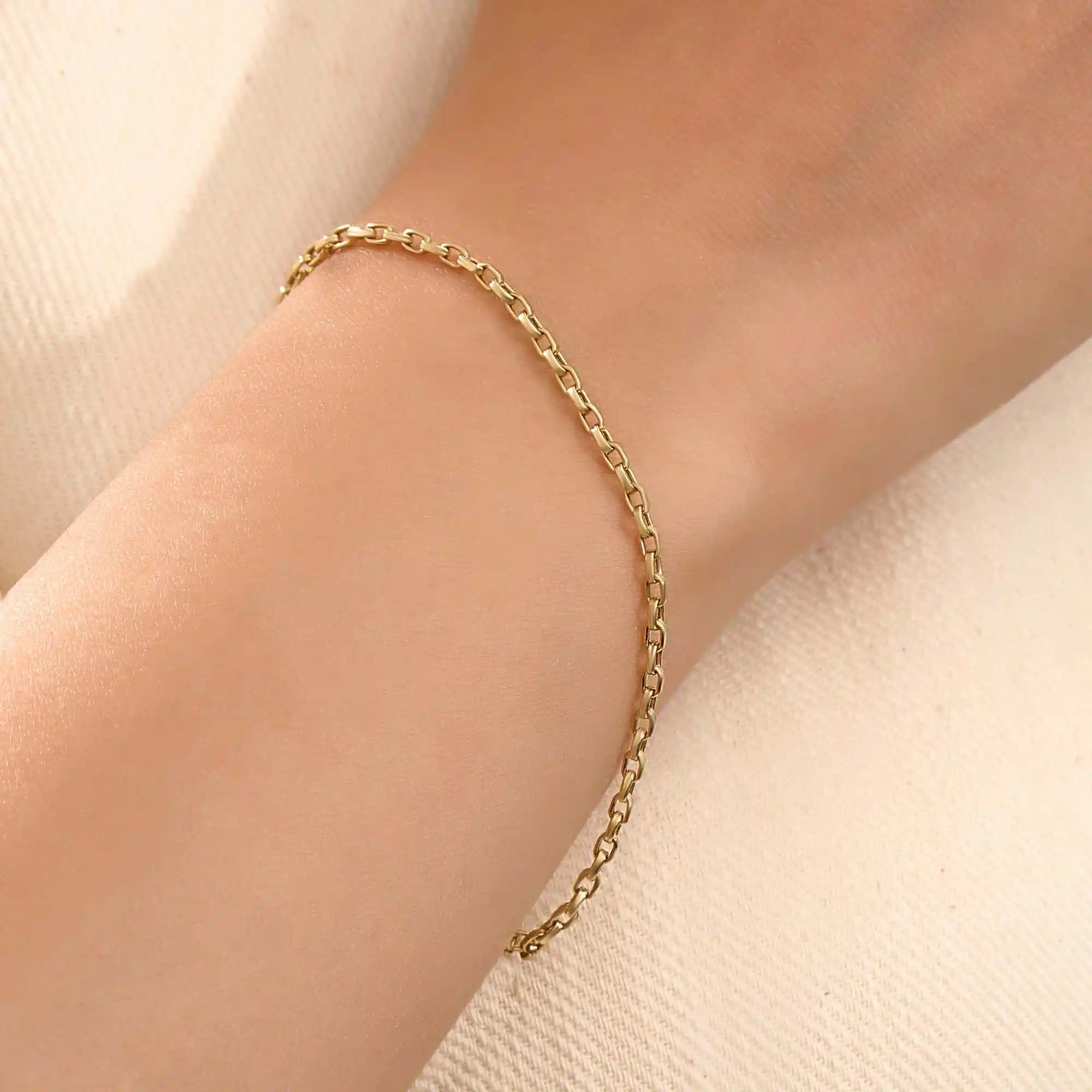 Model wearing a 14k gold rolo chain bracelet, showcasing the interlocking rectangular link design on the wrist.
