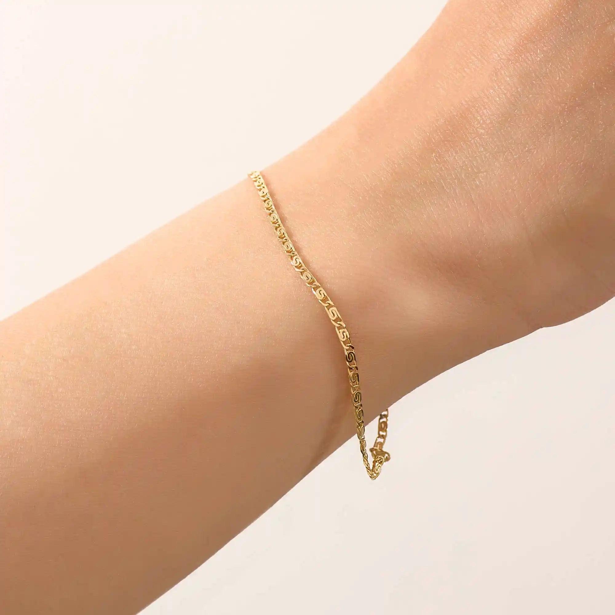 Model wearing a 14k gold scroll chain bracelet, showcasing the slim rectangular scroll link design on the wrist.

