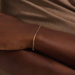 Model wearing a 14k gold scroll chain bracelet, showcasing the slim rectangular scroll link design on the wrist.
