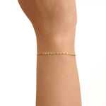 Model wearing a 14k gold scroll chain bracelet, showcasing the slim rectangular scroll link design on the wrist.
