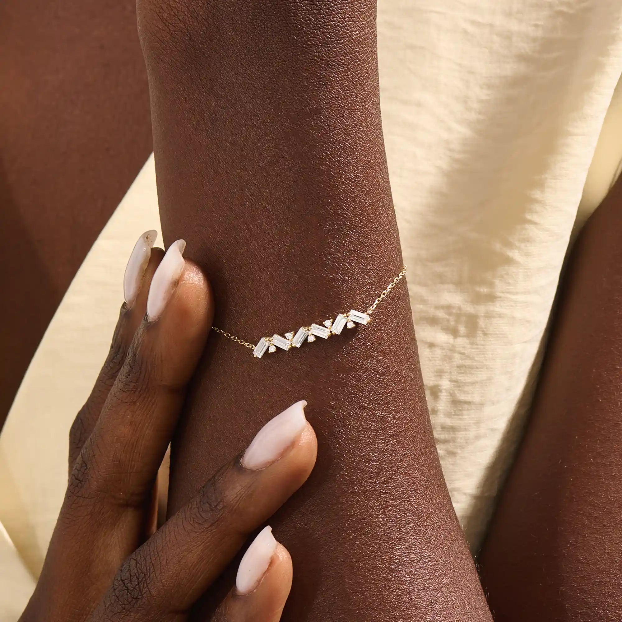 Model wearing a 14k yellow gold baguette bar bracelet with baguette-cut and round stones, adding sparkle to a refined wrist look.
