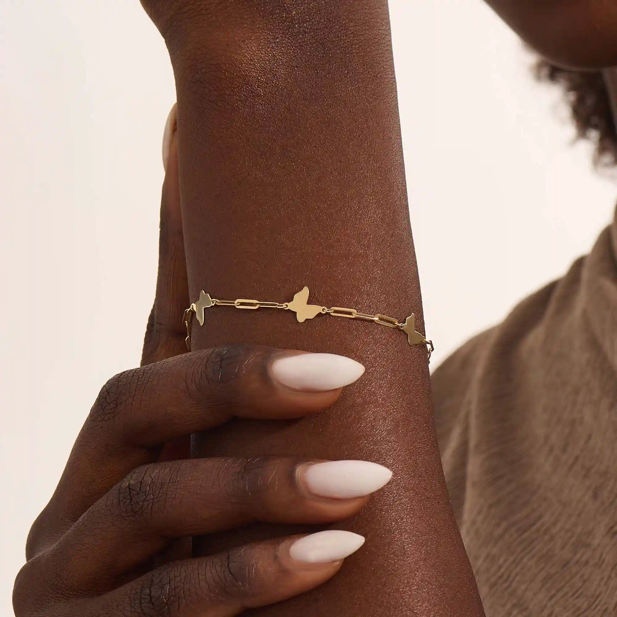 Model wearing a 14k yellow gold butterfly chain bracelet with polished butterfly charms and delicate chain details.
