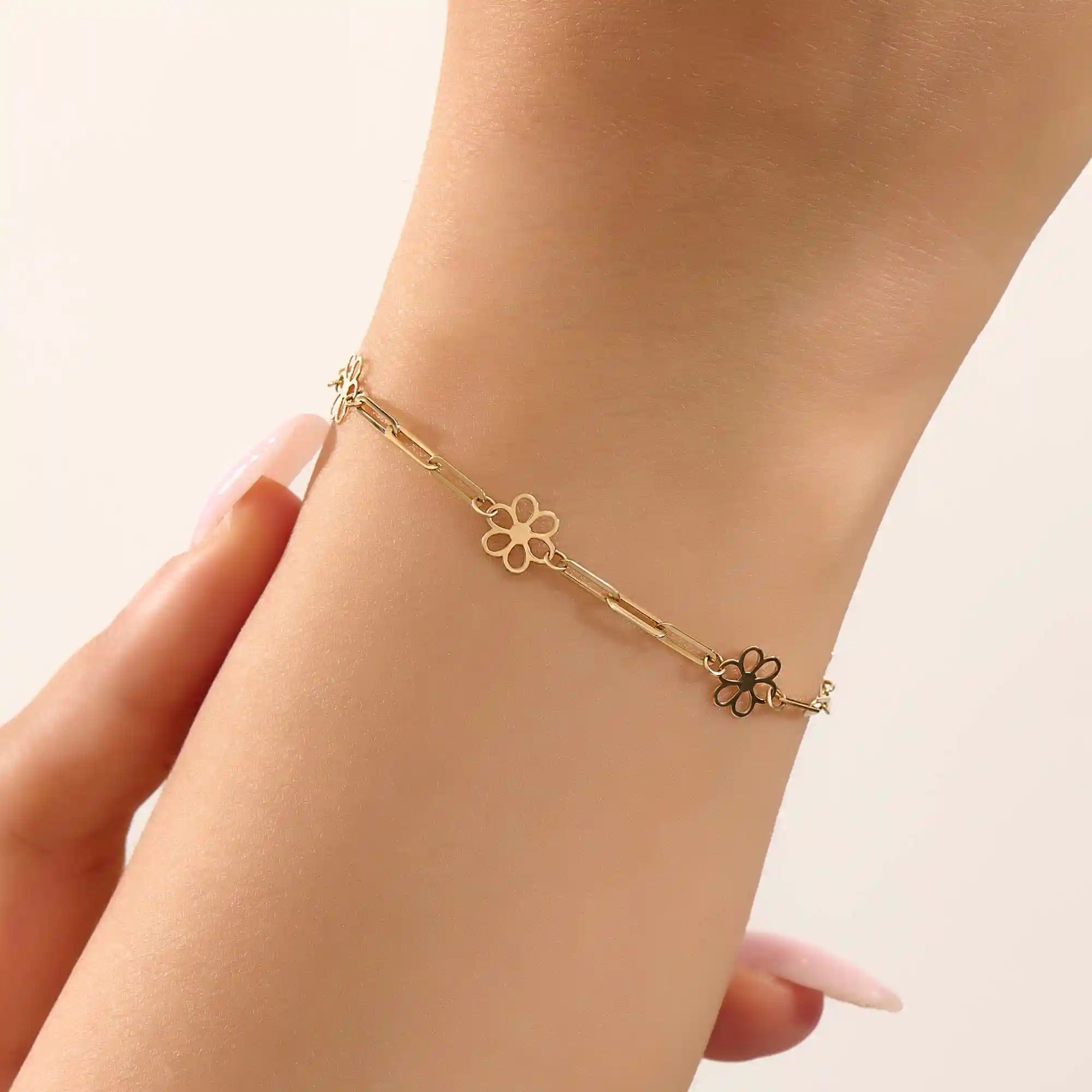 Model wearing a 14k yellow gold flower chain bracelet with delicate floral motifs for a soft, elegant style.
