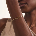 Model wearing a 14k yellow gold flower chain bracelet with delicate floral motifs for a soft, elegant style.
