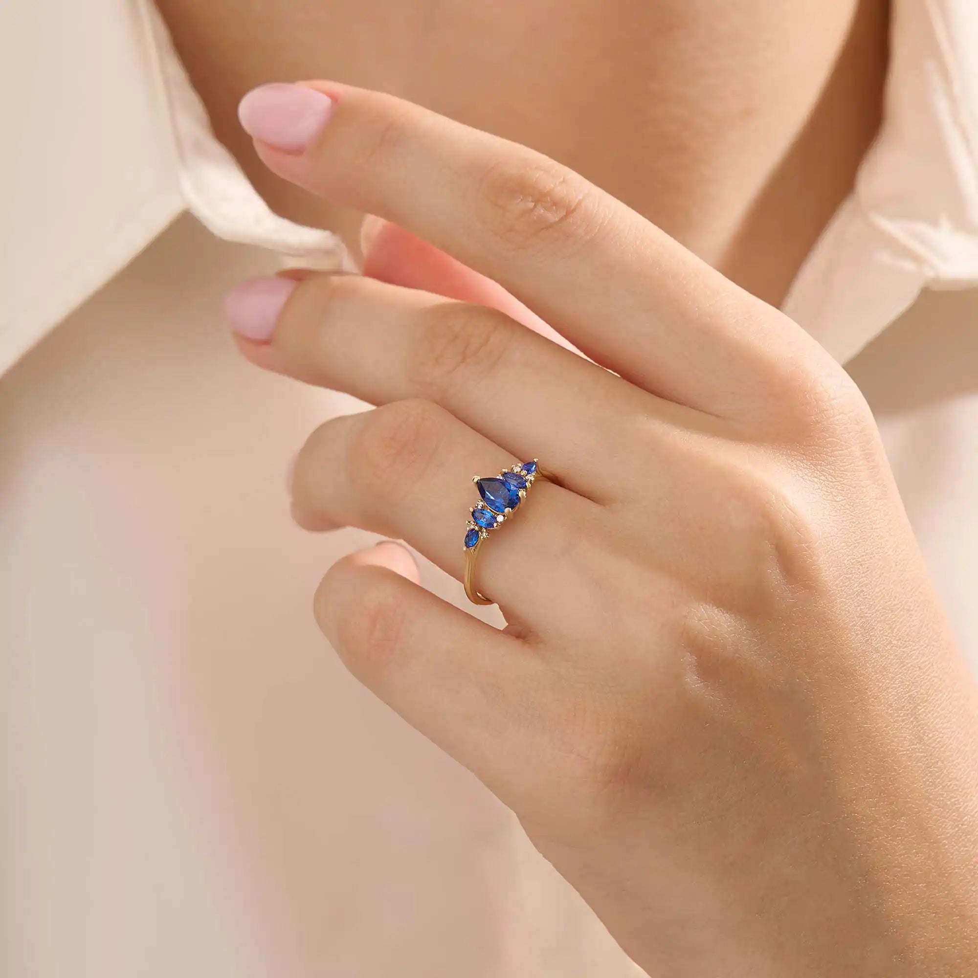 Model wearing a 5 pear sapphire gold ring on hand. Classic anniversary ring with vivid blue sapphires in 14k solid gold.