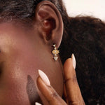 Model wearing dangling motif stud earrings in 14k gold, featuring moissanite-accented geometric star and triangle designs.
