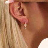 Model wearing dangling motif stud earrings in 14k gold, featuring moissanite-accented geometric star and triangle designs.
