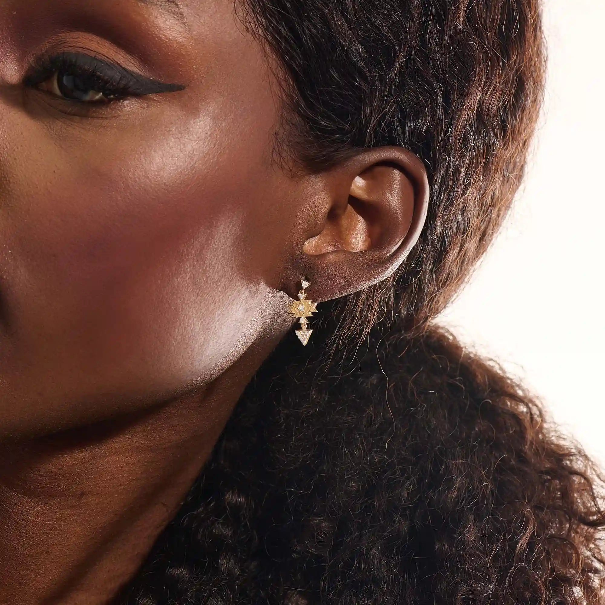 Model wearing dangling motif stud earrings in 14k gold, featuring moissanite-accented geometric star and triangle designs.

