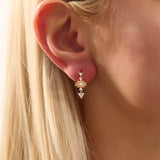 Model wearing dangling motif stud earrings in 14k gold, featuring moissanite-accented geometric star and triangle designs.
