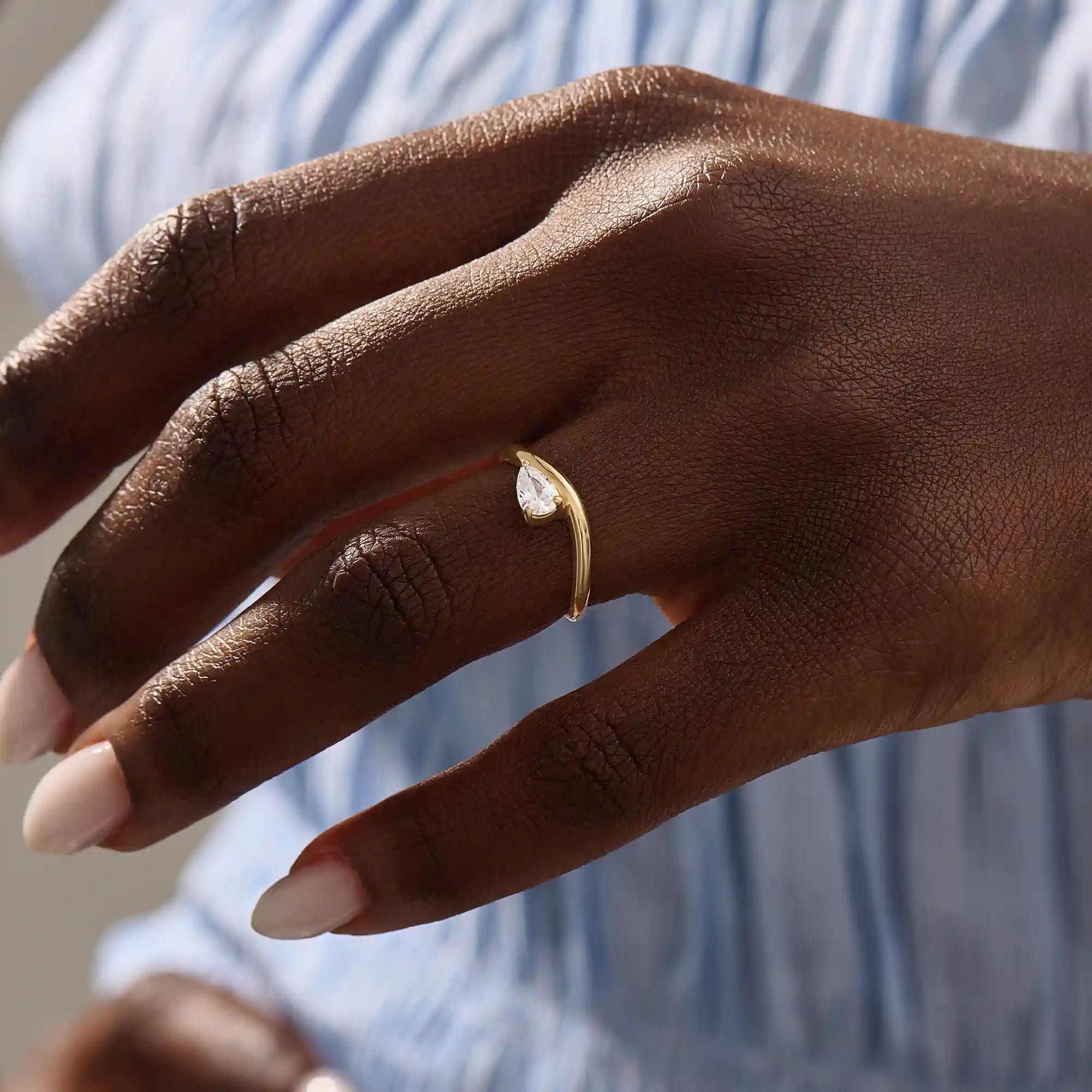 Model wearing pear cut moissanite solitaire engagement ring on a curved 14k solid gold band, highlighting its sleek and modern minimalist style.