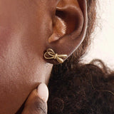 Model wearing simple ribbon stud earrings in 14k gold, showcasing their playful and elegant bow style.
