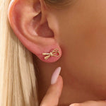 Model wearing simple ribbon stud earrings in 14k gold, showcasing their playful and elegant bow style.
