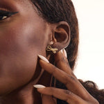 Model wearing simple ribbon stud earrings in 14k gold, showcasing their playful and elegant bow style.
