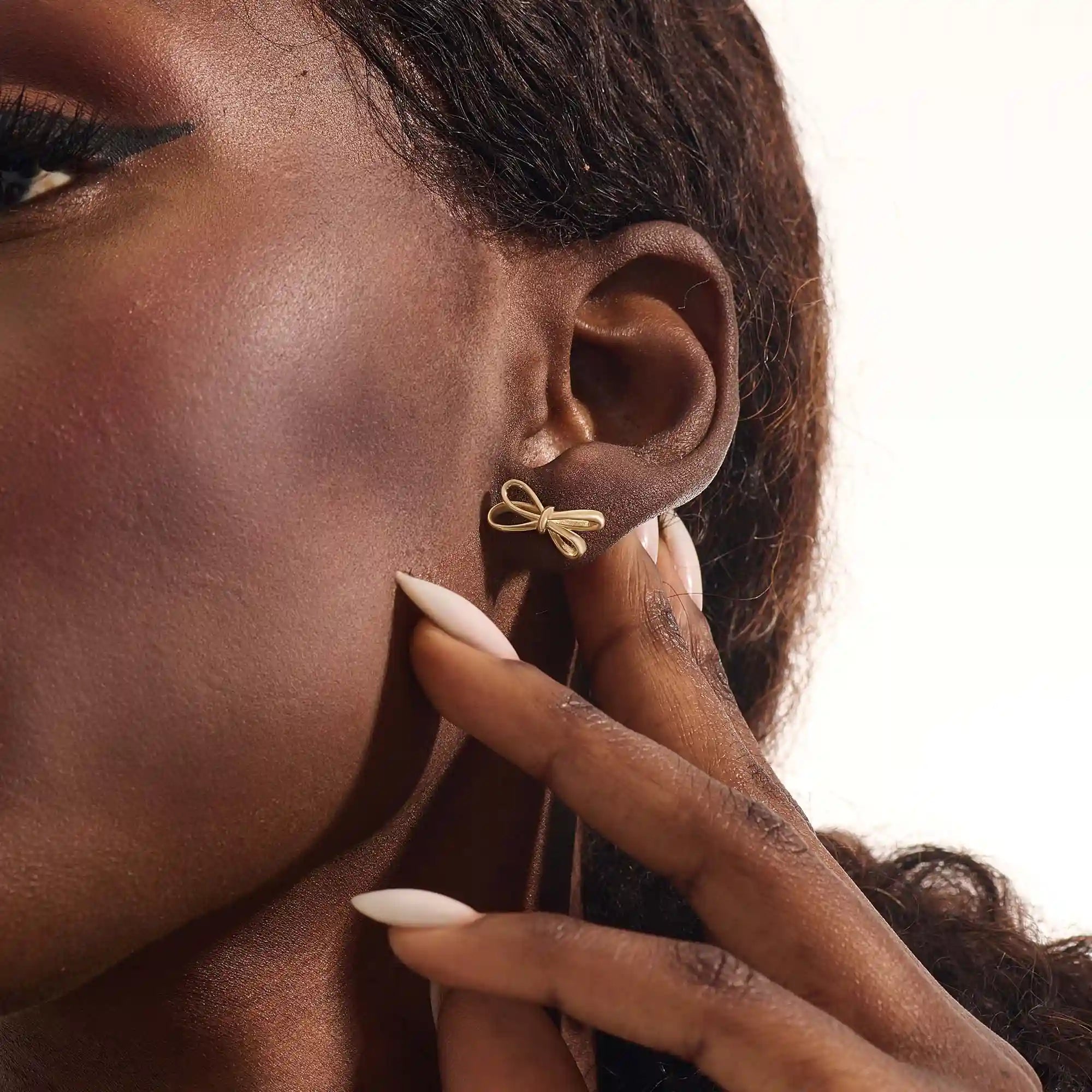 Model wearing simple ribbon stud earrings in 14k gold, showcasing their playful and elegant bow style.
